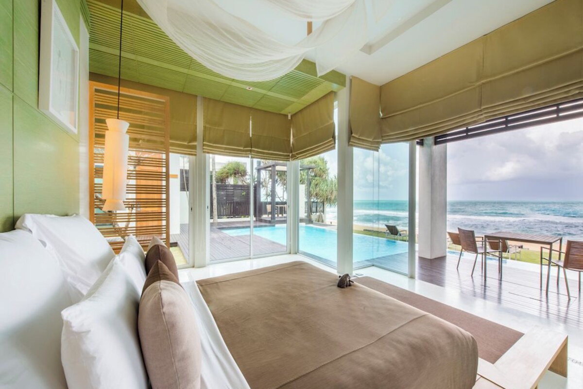 Quarto com uma cama grande, vista para o oceano e área de piscina.