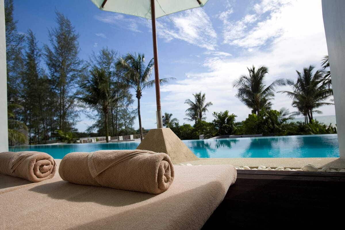 A poolside area with a view of a clear blue sky, palm trees, and a pool.