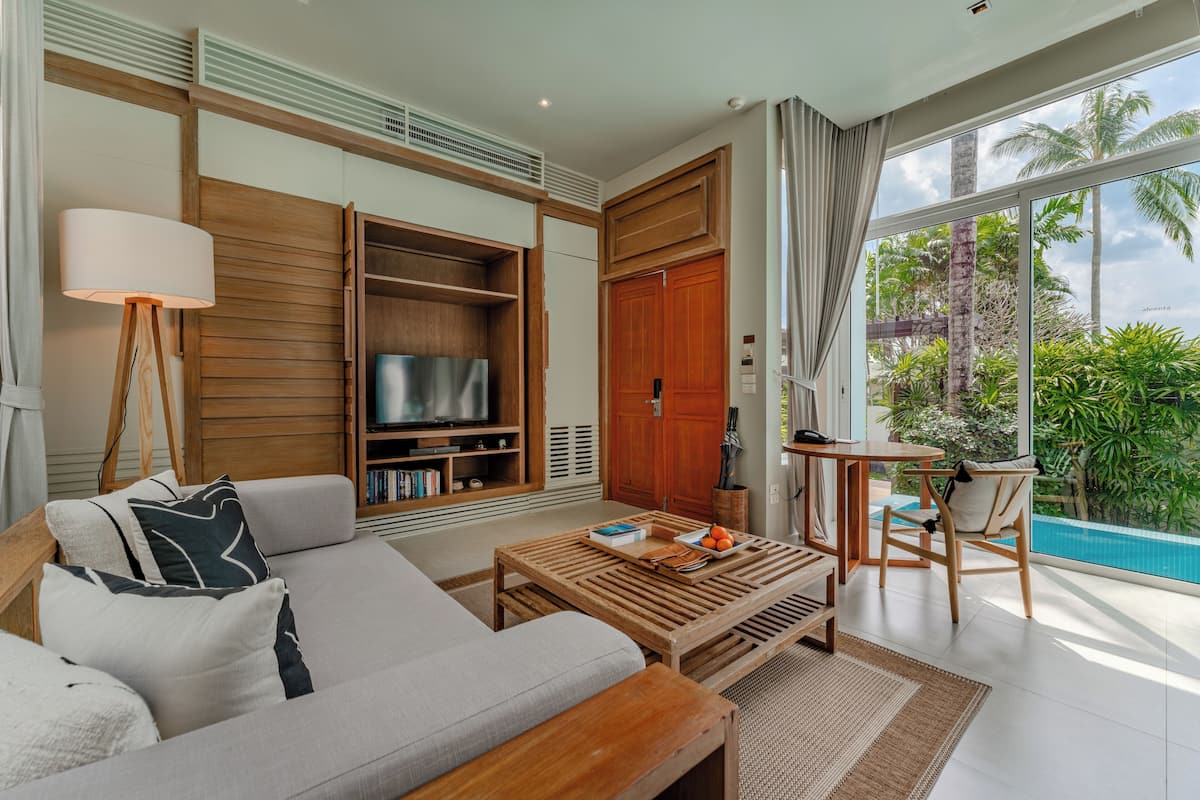 A modern living room with a sofa, coffee table, TV, and a view of a swimming pool.