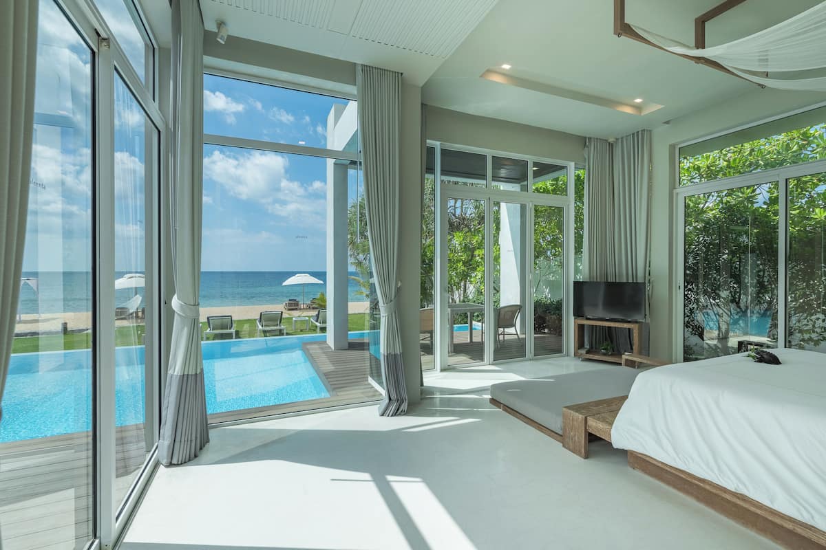 A modern bedroom with a large bed, a TV, and a view of the ocean.