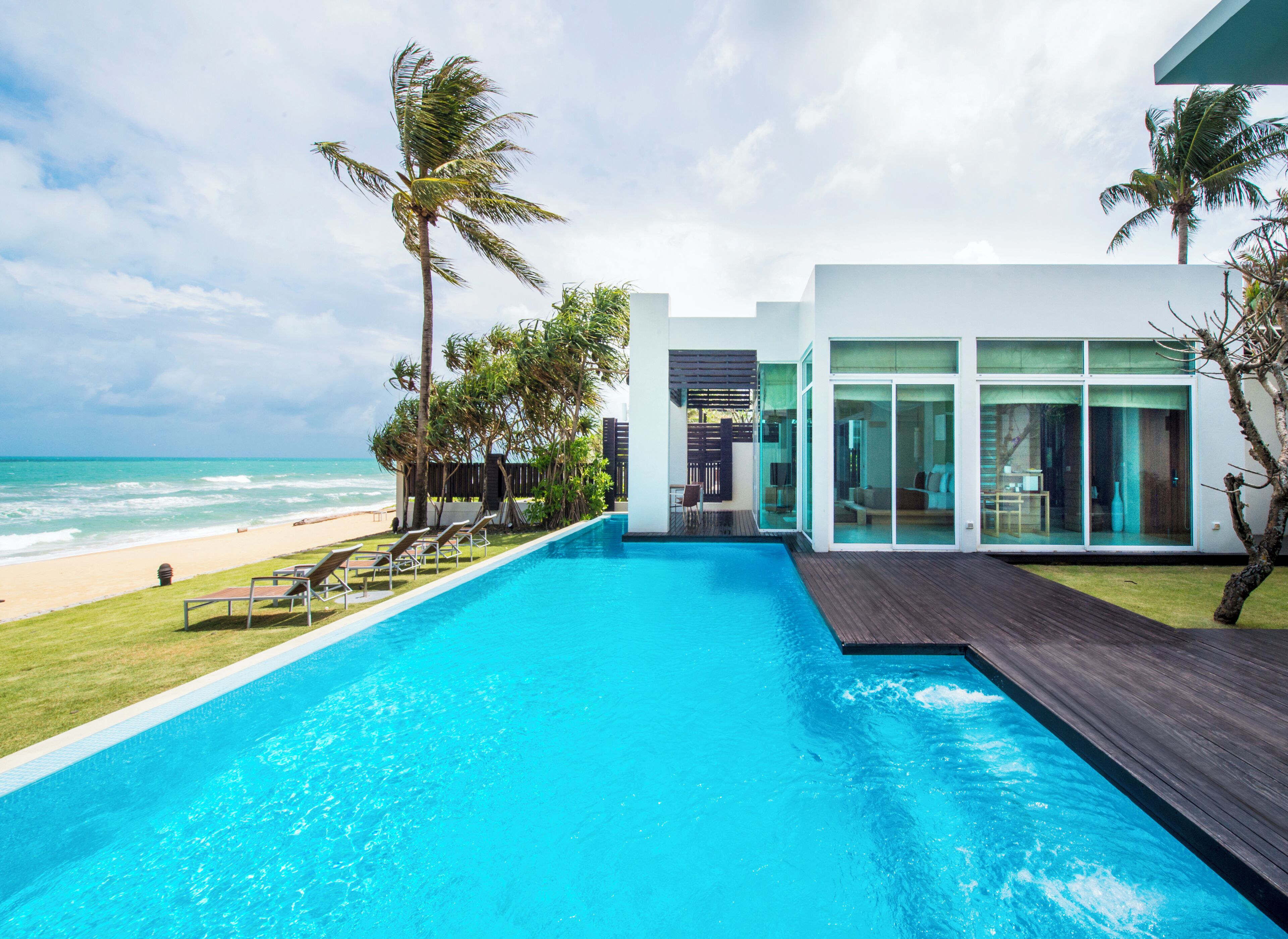 Ein moderner Poolbereich mit Meerblick, einer Holzterrasse und einem gläsernen Anbau.