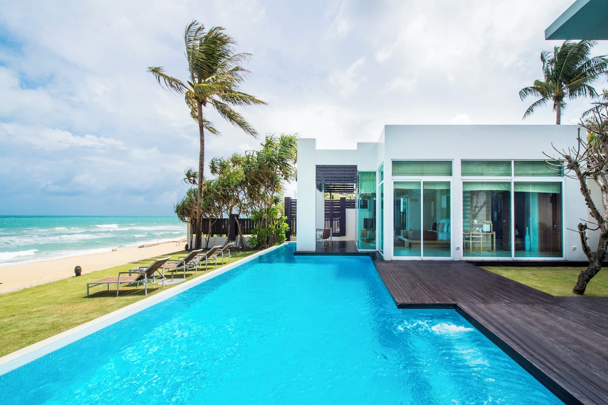 A modern poolside area with a view of the ocean, a wooden deck, and a glass-enclosed room.