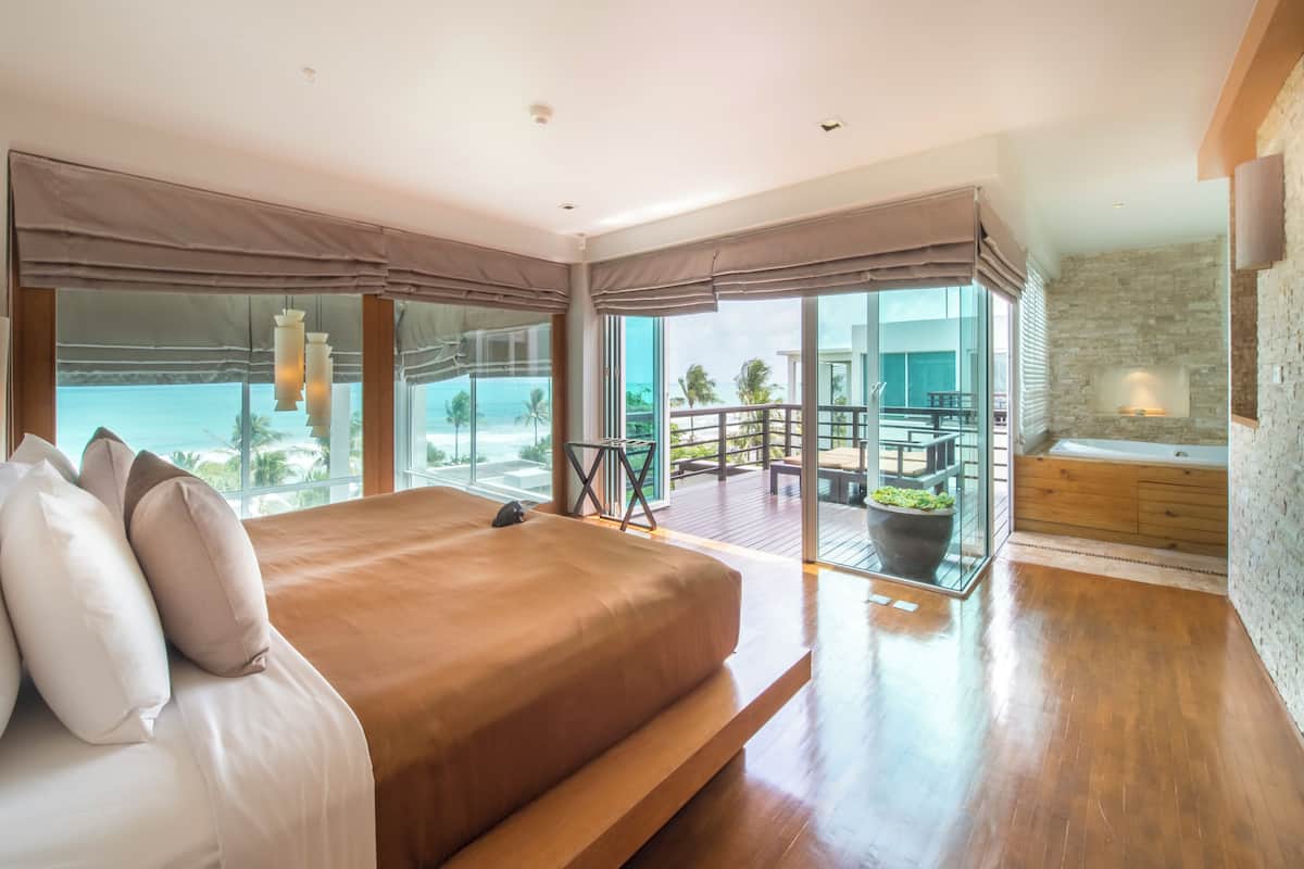 A modern bedroom with a large bed, a balcony with a view of the ocean, and a spa area with a bathtub.