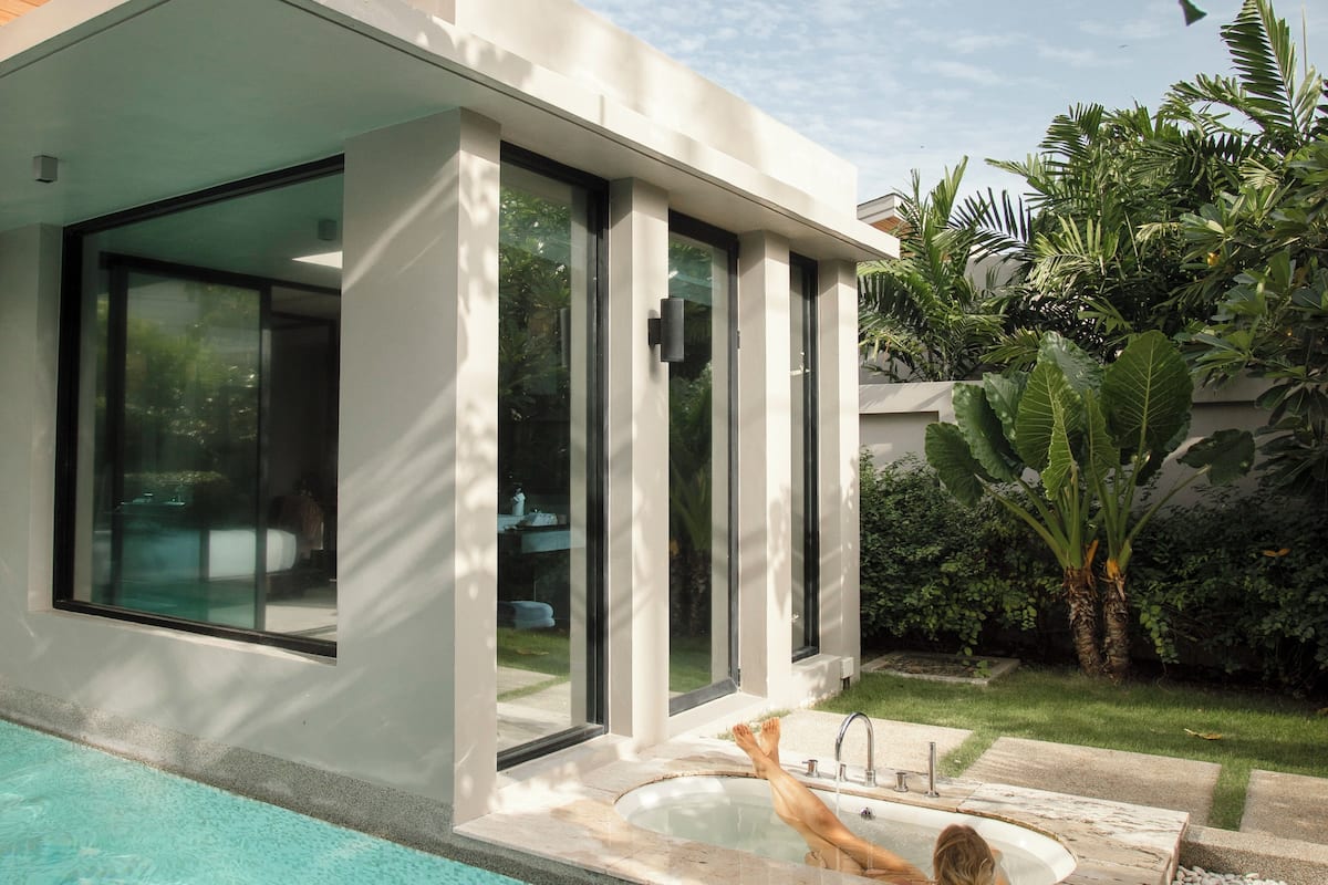 A modern house with a swimming pool, large glass doors, and a garden with tropical plants.