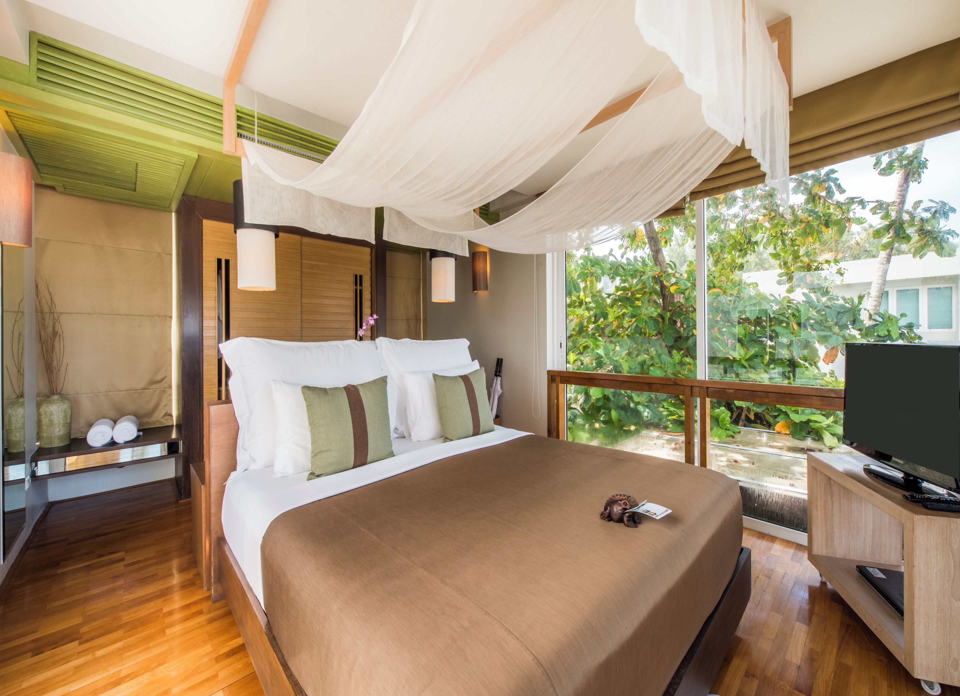 A bedroom with a large bed, a TV, and a view of greenery outside.