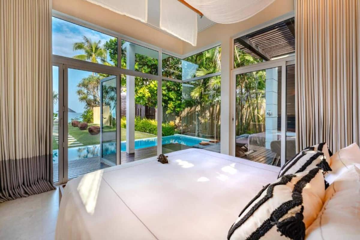 A modern bedroom with a large bed, a view of a swimming pool, and sliding glass doors leading to an outdoor area.