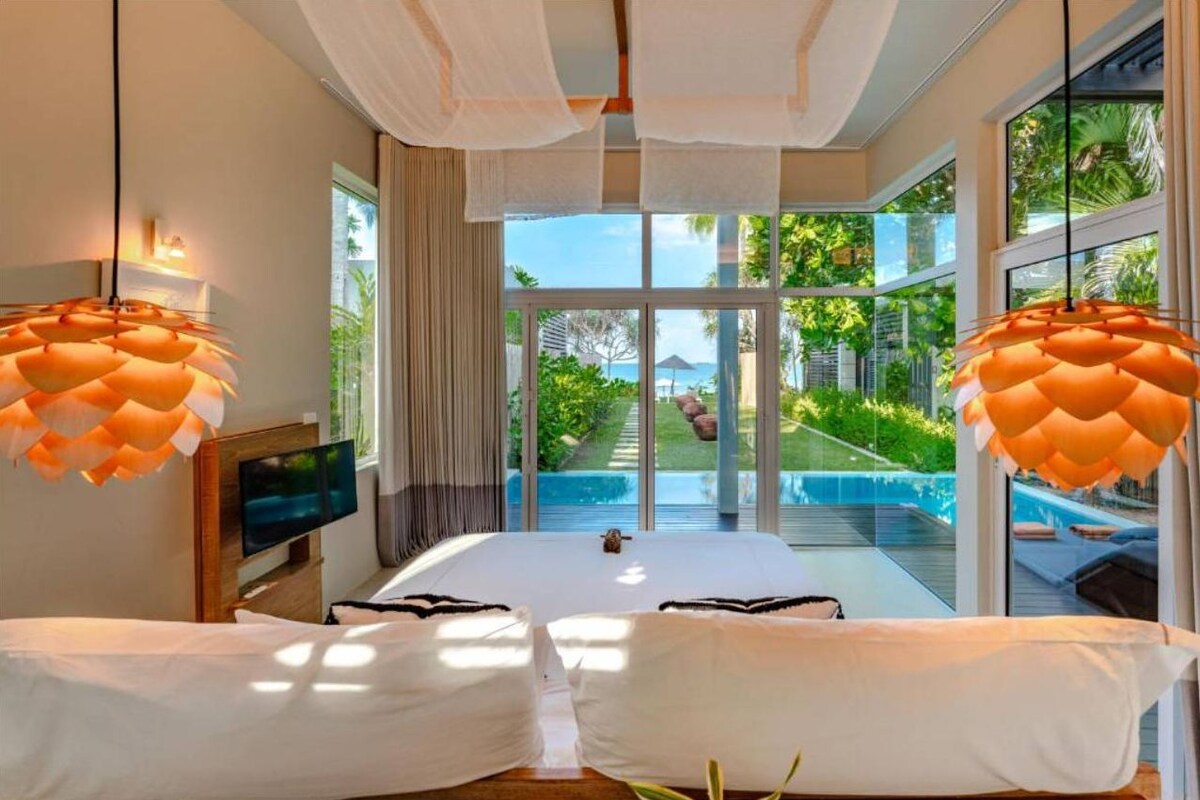Quarto com cama grande, televisão e vista para a piscina e jardim.