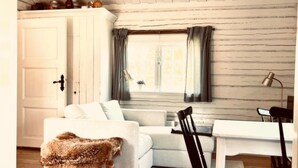 Une pièce avec un canapé blanc, un plaid en fourrure, une table à manger avec des chaises et une fenêtre avec des rideaux.