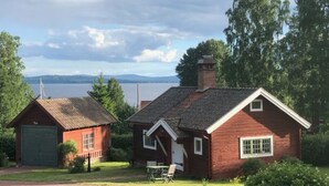 Une maison en bois rouge avec un garage, un petit porche et une vue sur un lac et des montagnes en arrière-plan.