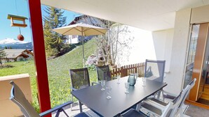 An outdoor dining area with a table, chairs, and a hanging light fixture. - 1508 Chesa Barlangia Setaria by Interhome (Valbella)