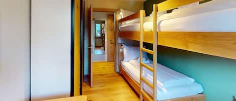 Une chambre avec des lits superposés, un plancher en bois et une porte donnant sur une autre pièce.