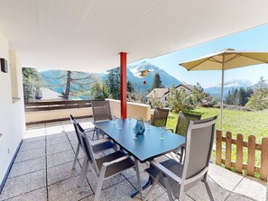 A patio with a table and chairs, a mountain view, and a wooden fence. - Apartment  by Interhome (Valbella)