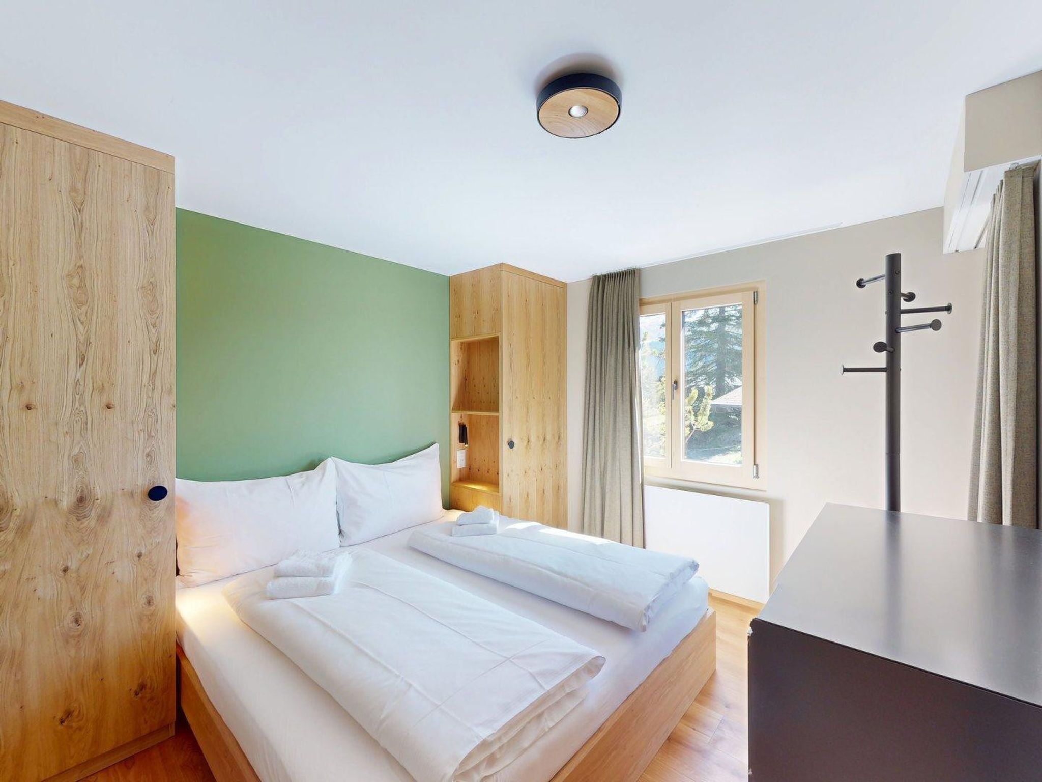 Ein Hotelzimmer mit einem Bett, einem Holzschrank, einem Schreibtisch und einem Fenster mit Vorhängen.