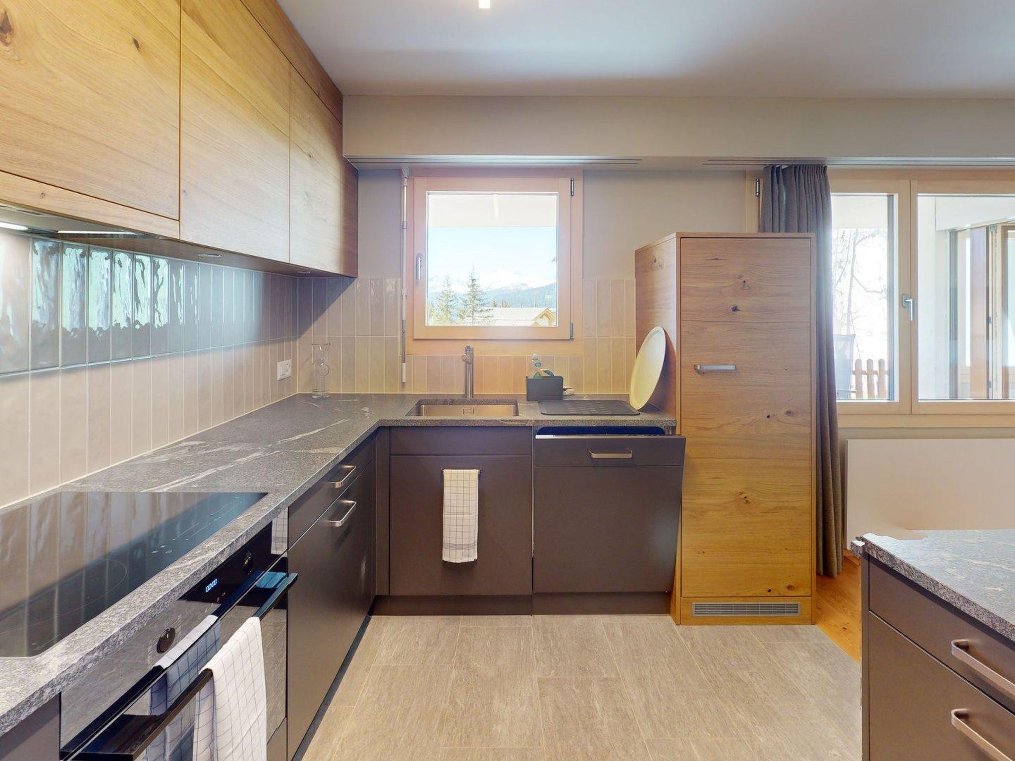 A modern kitchen with a built-in oven, a sink, and a window with a view of the outdoors.