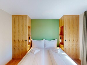 Een slaapkamer met een bed, groene wanden, houten kasten en een gordijn.