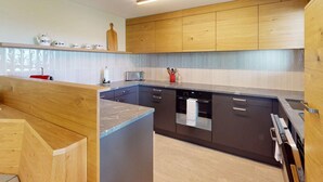 A modern kitchen with wooden cabinets, a central island, and a built-in dishwasher. - 1508 Chesa Barlangia Setaria by Interhome (Valbella)