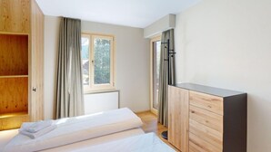 A bedroom with a bed, wooden wardrobe, and a window with curtains. - 1508 Chesa Barlangia Setaria by Interhome (Valbella)