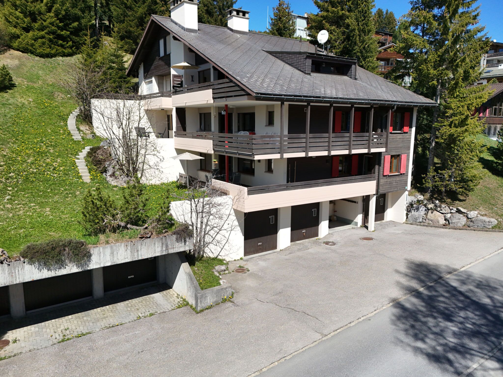 En byggnad med flera våningar, ett sluttande tak, flera balkonger och en uppfart som leder till ett garage.