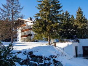 A modern multi-story building with a snow-covered landscape, surrounded by evergreen trees. - 1506 Casoja Valbella by Interhome (Valbella)