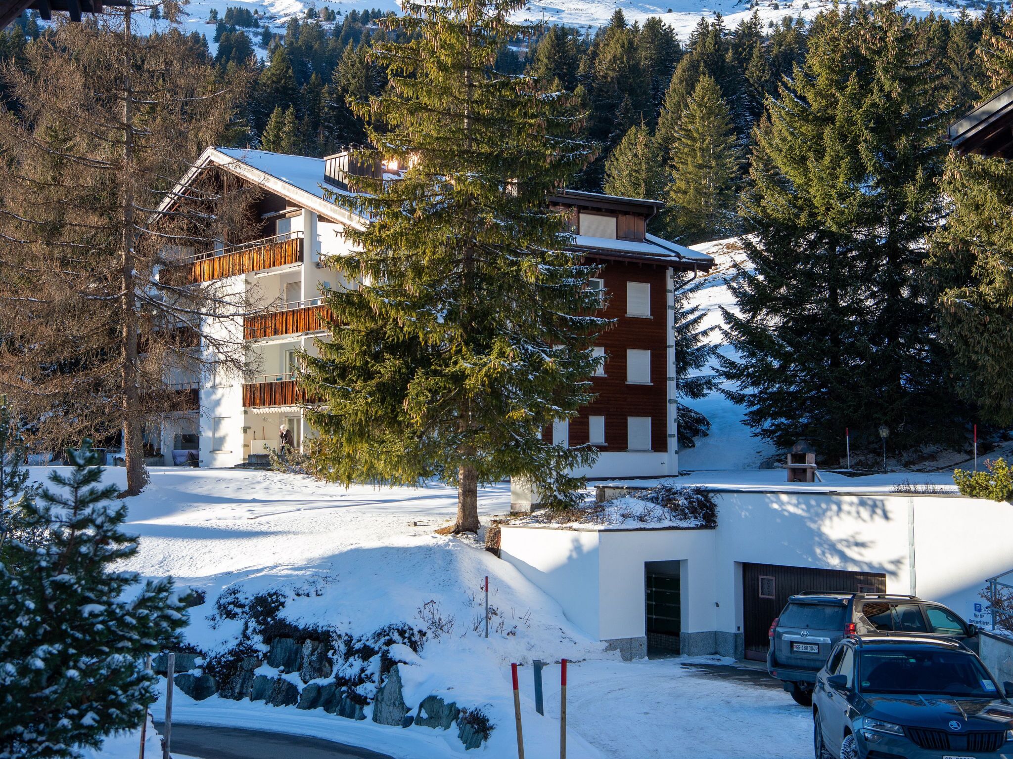 A multi-story building with a snow-covered roof, surrounded by trees and a clear sky.