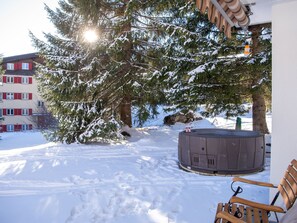 A snow-covered outdoor area with a hot tub, a wooden bench, and a building with red shutters. - 1506 Casoja Valbella by Interhome (Valbella)