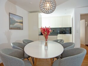 A modern dining area with a round table, grey upholstered chairs, and a vase with dried flowers. - 1506 Casoja Valbella by Interhome (Valbella)