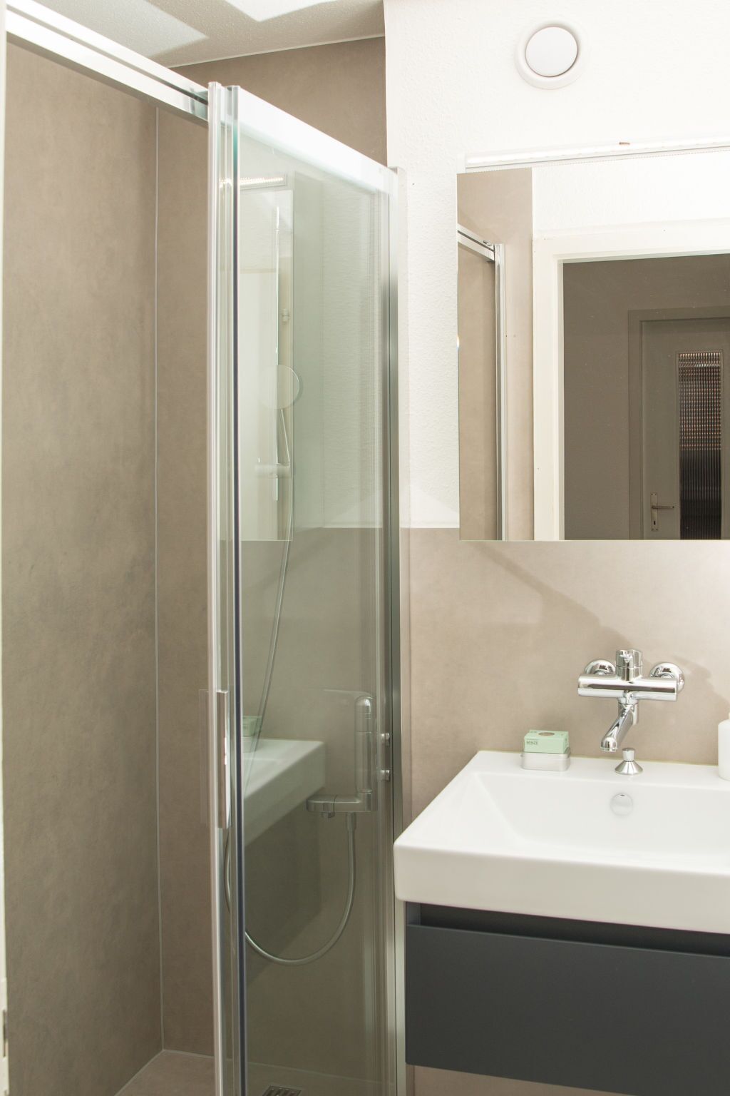 Un baño moderno con ducha envuelta en vidrio, un lavamanos blanco y un espejo sobre él.