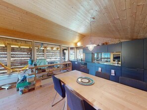 Un intérieur en bois comprenant une table à manger, des chaises et un coin cuisine avec des placards et un réfrigérateur.