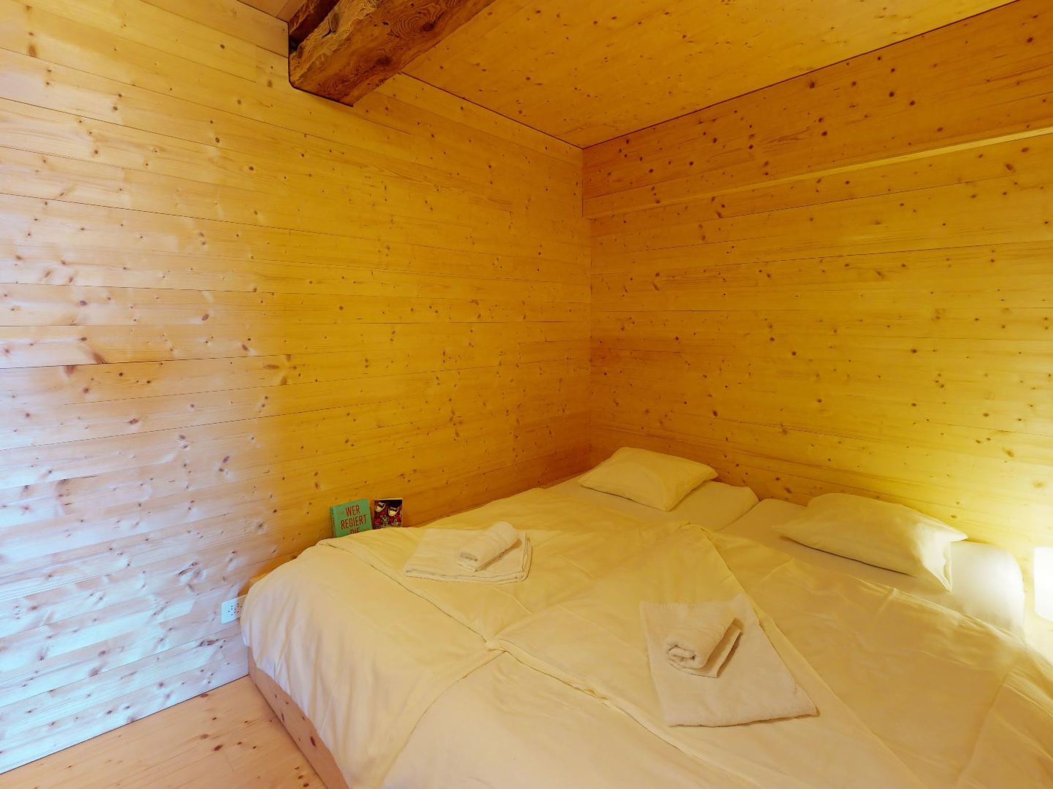 Ein Zimmer mit Holzwänden und einem Bett mit weißer Bettwäsche.