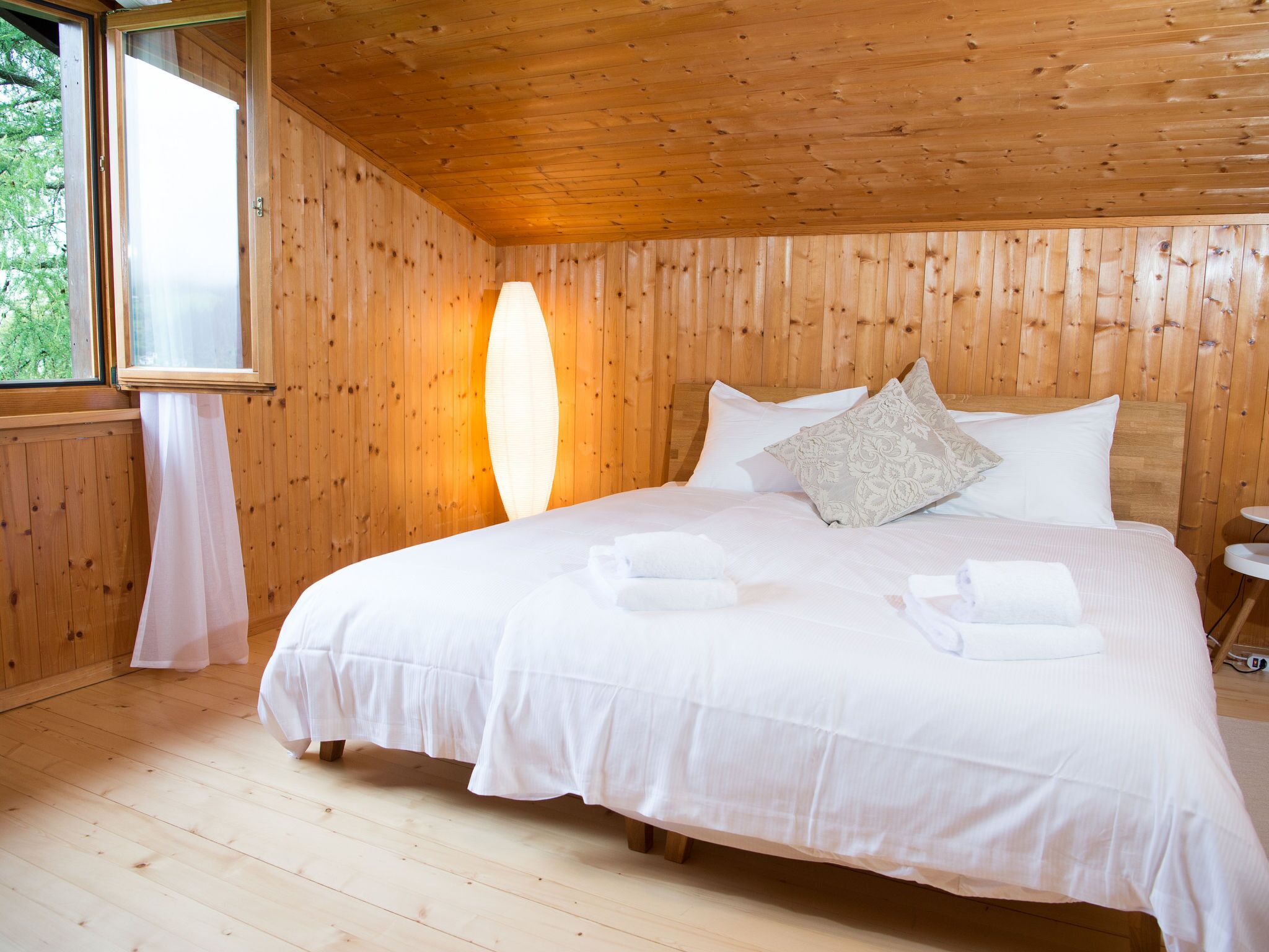 Een houten kamer met een bed, kussens en een raam.