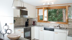 A modern kitchen with white cabinets, a built-in oven, a coffee maker, and a window with a view of trees. - 1301 Haus Joch by Interhome (Churwalden)