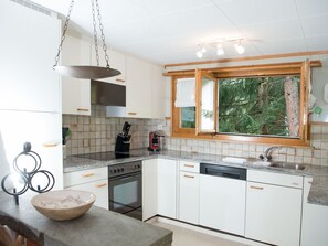 A modern kitchen with white cabinets, a built-in oven, a coffee maker, and a window with a view of trees. - 1301 Haus Joch by Interhome (Churwalden)