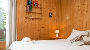 A wooden-paneled room with a bed, a nightstand with a lamp, and a shelf with books. - 1301 Haus Joch by Interhome (Churwalden)