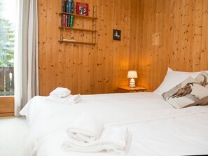 A wooden-paneled room with a bed, a nightstand with a lamp, and a shelf with books. - 1301 Haus Joch by Interhome (Churwalden)