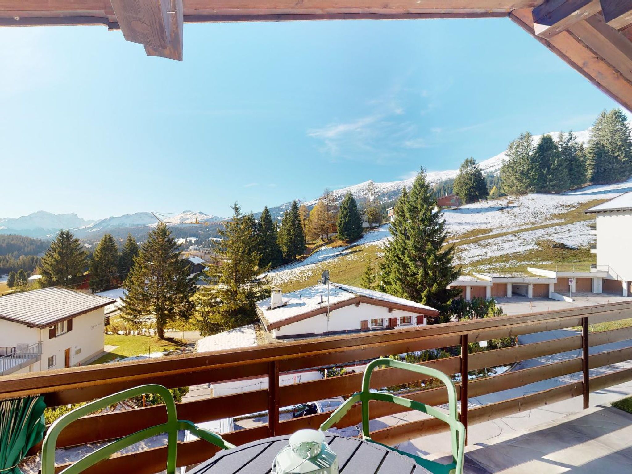 Un balcón con vista a una montaña nevada, una terraza de madera y un edificio con fachada blanca.