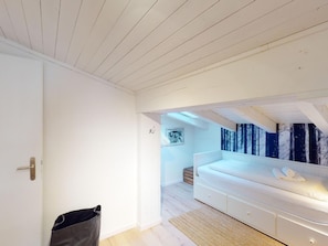 Ein Schlafzimmer mit einem weißen Bett, Holzboden und einem großen Fenster mit Blick auf einen Wald.