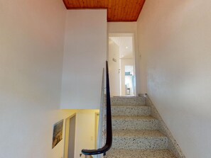 Eine Treppe mit Handlauf führt zu einer Zwischenebene, links eine Tür und dahinter ein Flur.