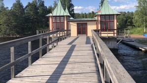 A wooden pier leading to a building with two green roofs and red doors. - Summer House Sweden in Rättvik for 9 people by Interhome (Rättvik)