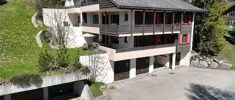 A multi-story building with a sloped roof, multiple balconies, and a driveway leading to a garage.