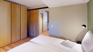 Quarto com cama, guarda-roupa de madeira e porta para outro cômodo.