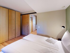 A bedroom with a bed, wooden wardrobe, and a door leading to another room.