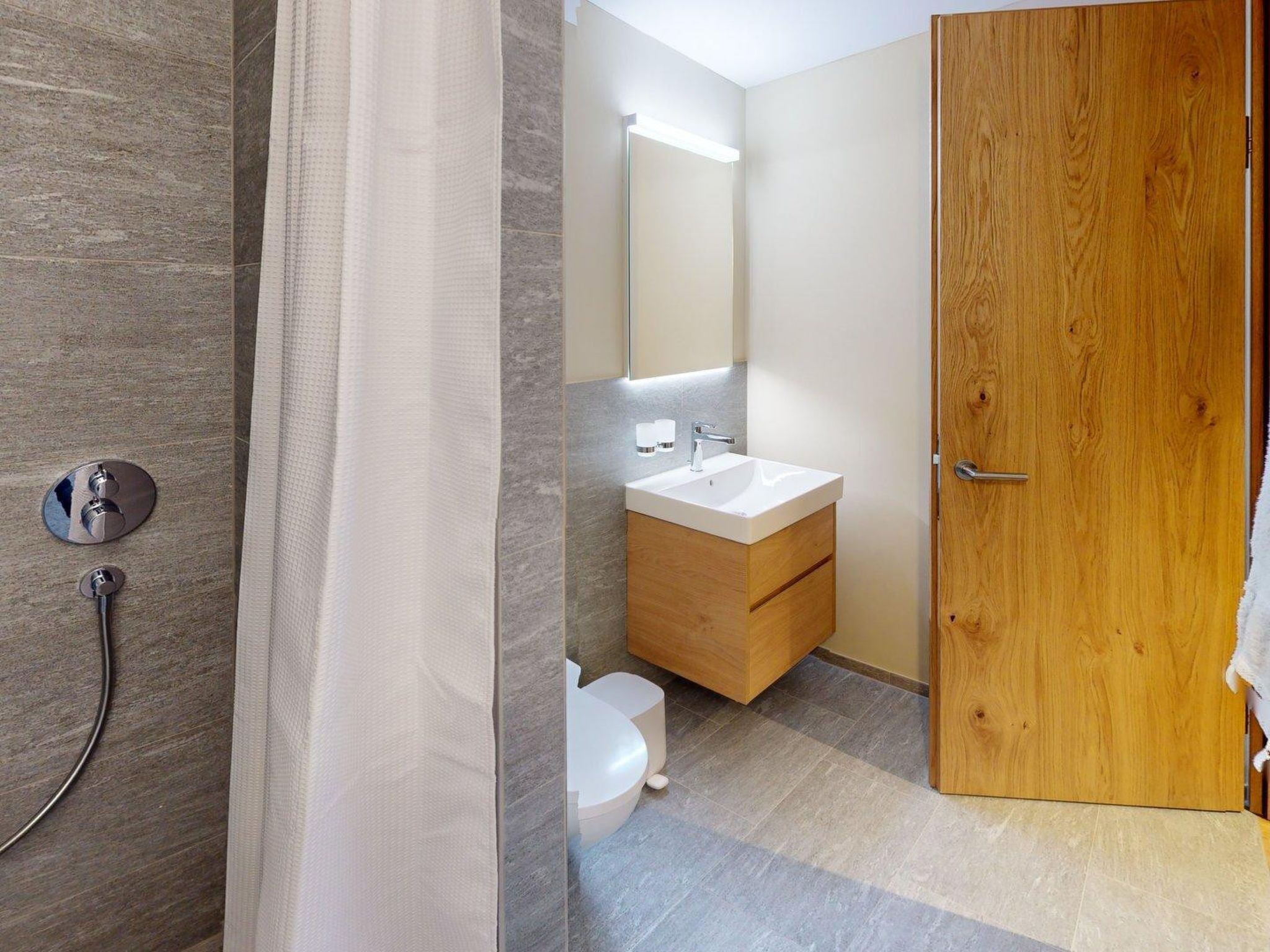 Une salle de bain avec douche, toilettes, lavabo et porte en bois.