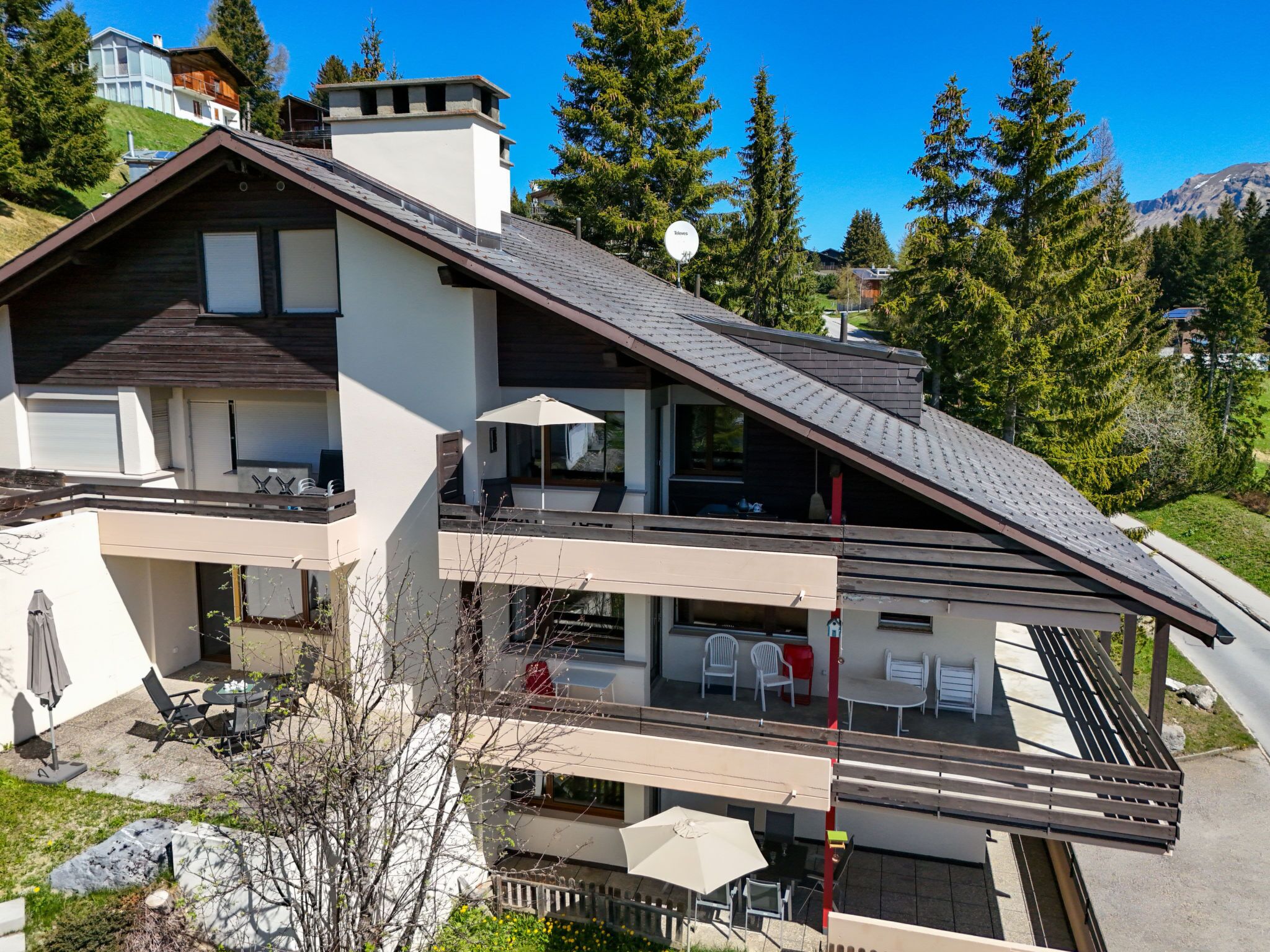 A modern two-story building with a sloped roof, balconies, and outdoor seating areas.