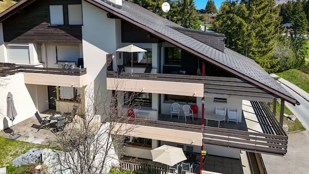 Um edifício moderno de dois andares com telhado inclinado, varandas e áreas de estar ao ar livre.