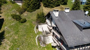 Uma casa moderna de dois andares com telhado inclinado, antena parabólica visível e um pátio pavimentado.