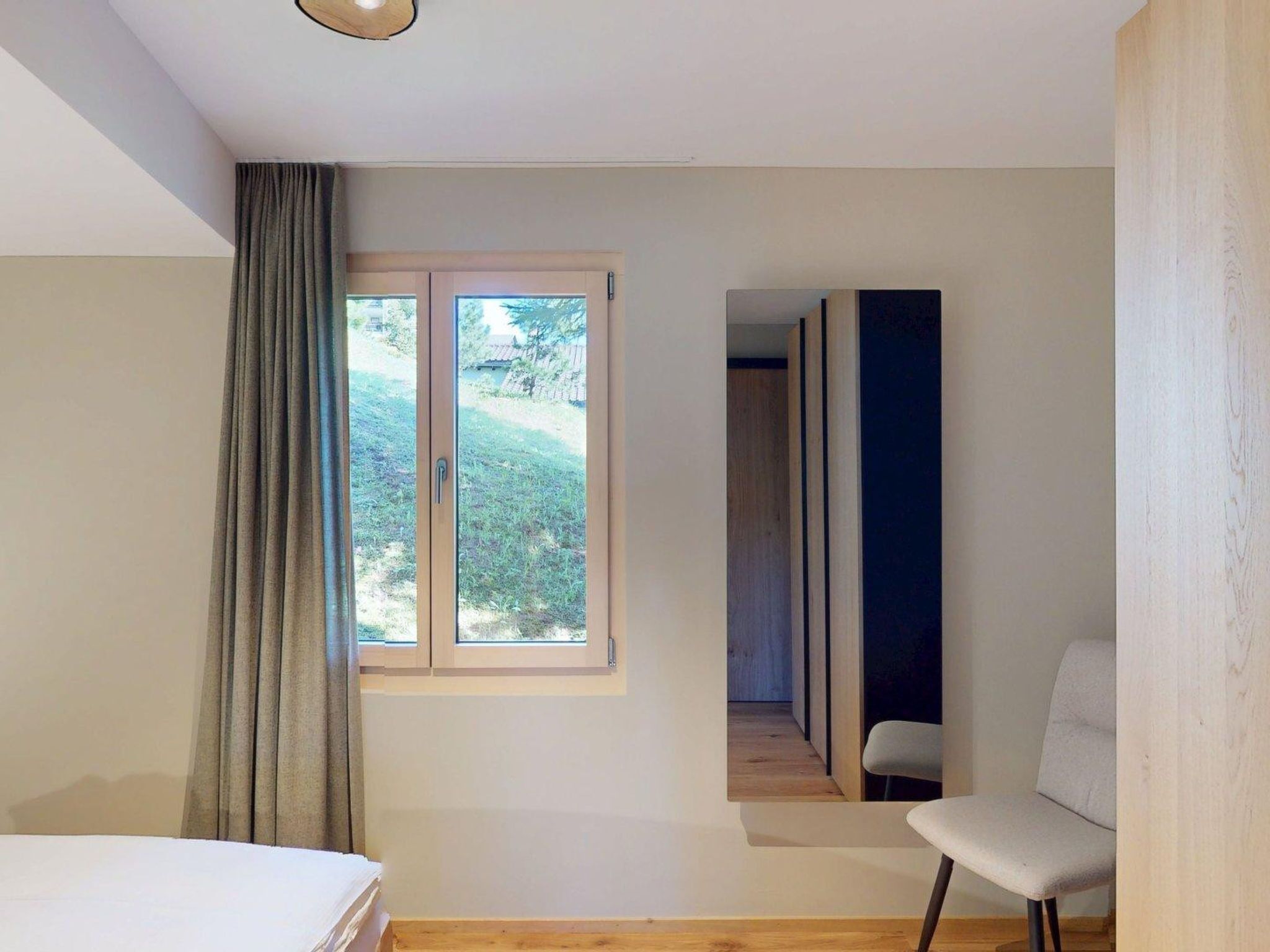 Ein Schlafzimmer mit einem Bett, einem fensterbelaubten Fenster, einem Sessel und Blick auf einen Garten.