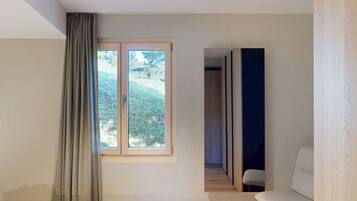 Ein Schlafzimmer mit einem Bett, einem fensterbelaubten Fenster, einem Sessel und Blick auf einen Garten.