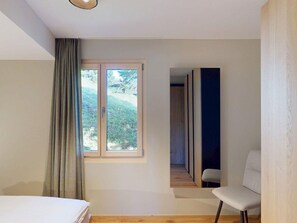A bedroom with a bed, a window with curtains, a chair, and a view of a garden. - 1509 Chesa Barlangia Molinia by Interhome (Valbella)