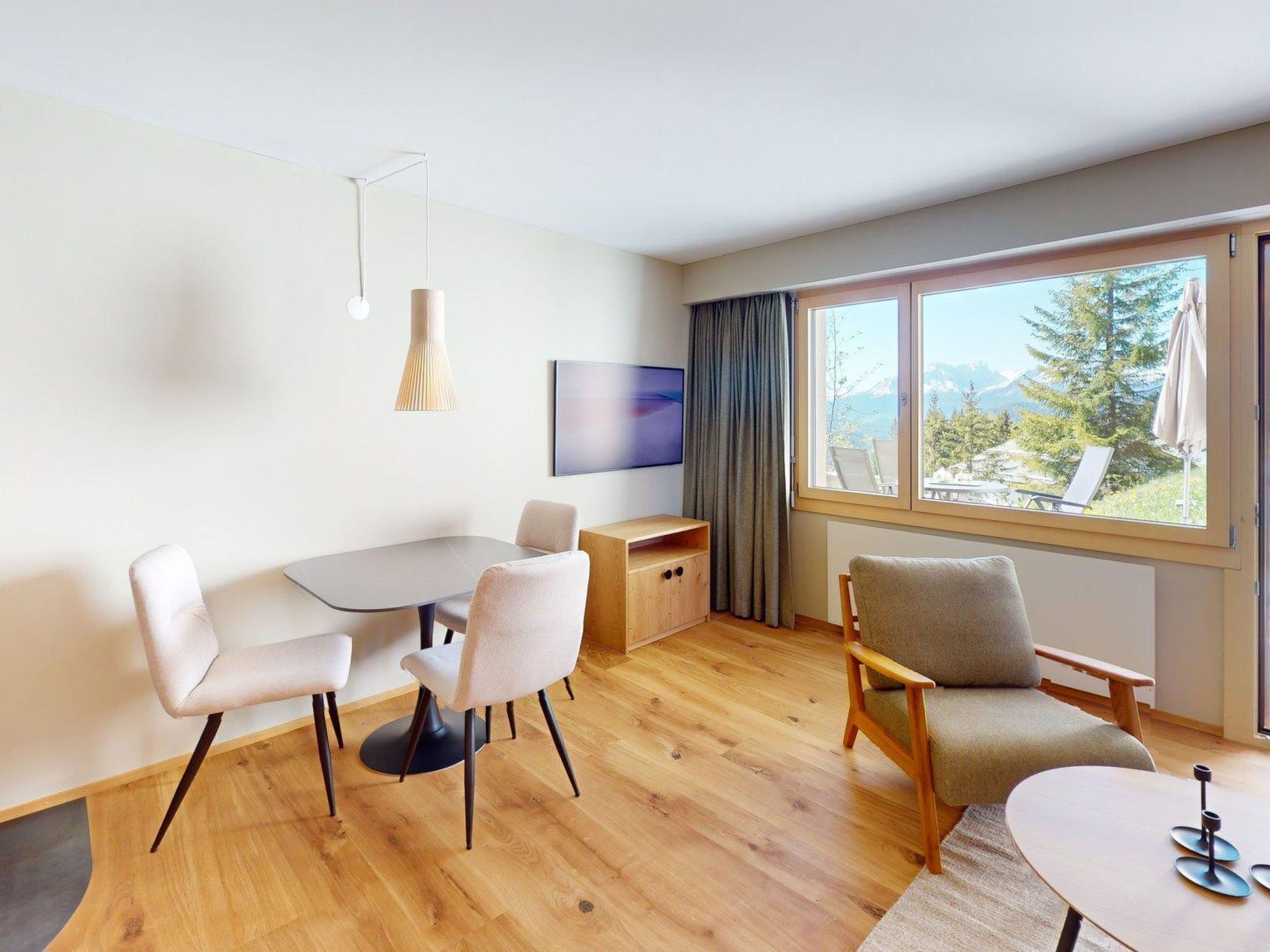 Una habitación moderna con una mesa de comedor, dos sillas, un sofá, un televisor y un ventanal con vistas a la montaña.
