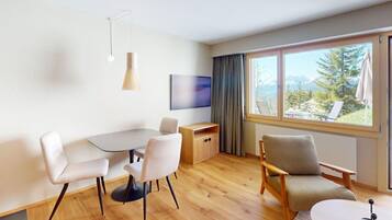 Una habitación moderna con una mesa de comedor, dos sillas, un sofá, un televisor y un ventanal con vistas a la montaña.